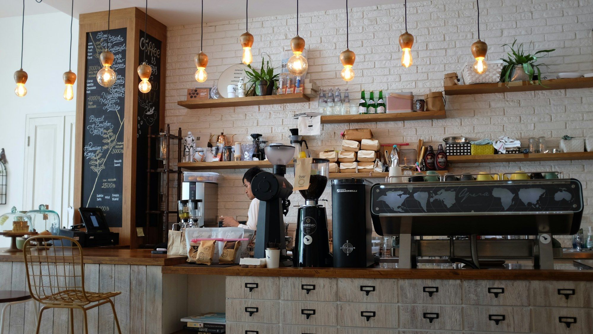 Café-Theke mit Siebträgermaschine, Hängelampen und Regalen voller Kaffee und Gläser